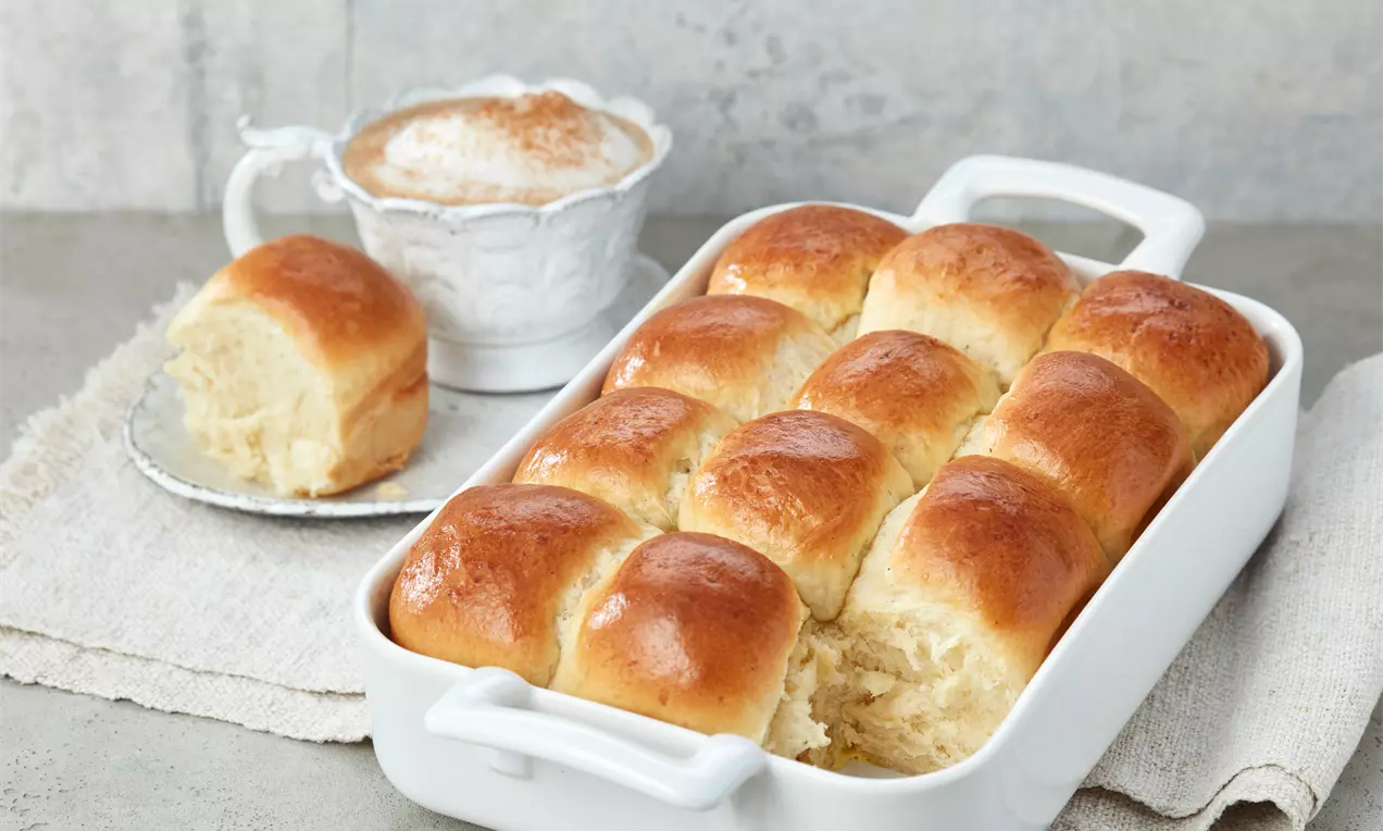 Milchbrötchen mit goldbrauner Kruste und sichtbarer fluffiger, heller Innenfläche, leicht mit Puderzucker bestäubt auf weißem Teller
