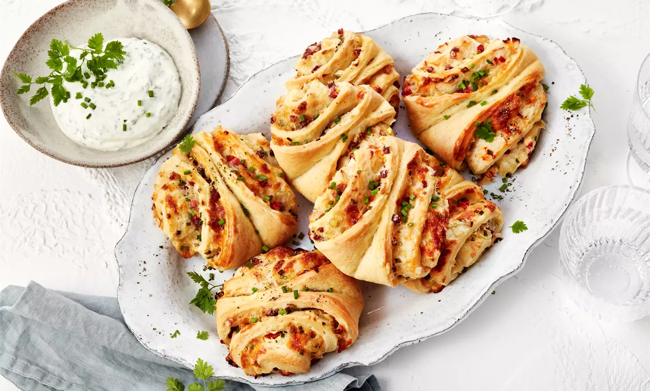 Flammkuchen-Franzbrötchen mit goldbraunem Teig, karamellisiertem Zimt-Zucker, saftigem Rahm und knusprigem Speck auf Holzbrett angerichtet